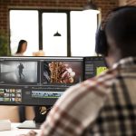 Rear view of male editor adjusting transitions and color grades during post production. African american creative professional wearing headphones while editing video footage at home studio.